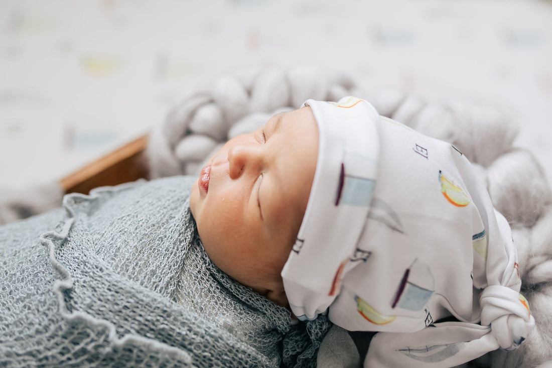 Newborn sleeping in their sailboat swaddle blanket and wearing their matching personalized sailboat hat.