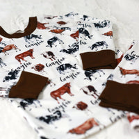 Our personalized cow pajamas folded nicely on a bed. The design has brown cows with white spots and black cows with spot spots.