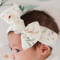 A close-up of a baby's head wearing a white floral headband with the name "Rose" printed on it.