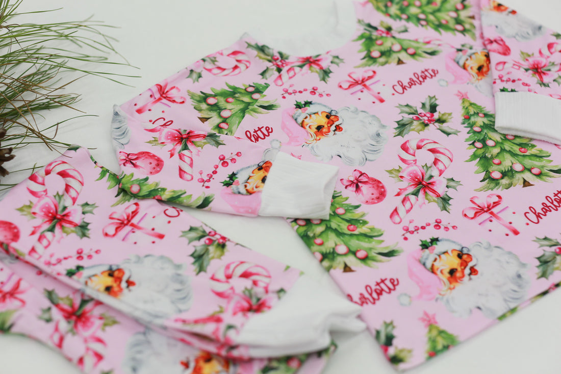 custom holiday sleepwear for little girls, with vintage santa faces and christmas trees with pink bows on a light pink material, name in red script font, and white cuffs.