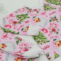 custom holiday sleepwear for little girls, with vintage santa faces and christmas trees with pink bows on a light pink material, name in red script font, and white cuffs.