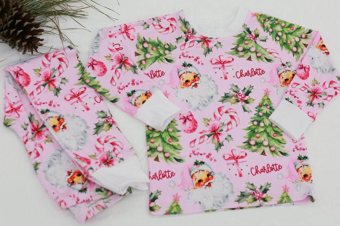 custom holiday sleepwear for little girls, with vintage santa faces and christmas trees with pink bows on a light pink material, name in red script font, and white cuffs.