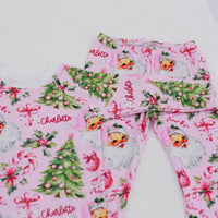 custom holiday sleepwear for little girls, with vintage santa faces and christmas trees with pink bows on a light pink material, name in red script font, and white cuffs.