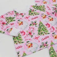 custom holiday sleepwear for little girls, with vintage santa faces and christmas trees with pink bows on a light pink material, name in red script font, and white cuffs.