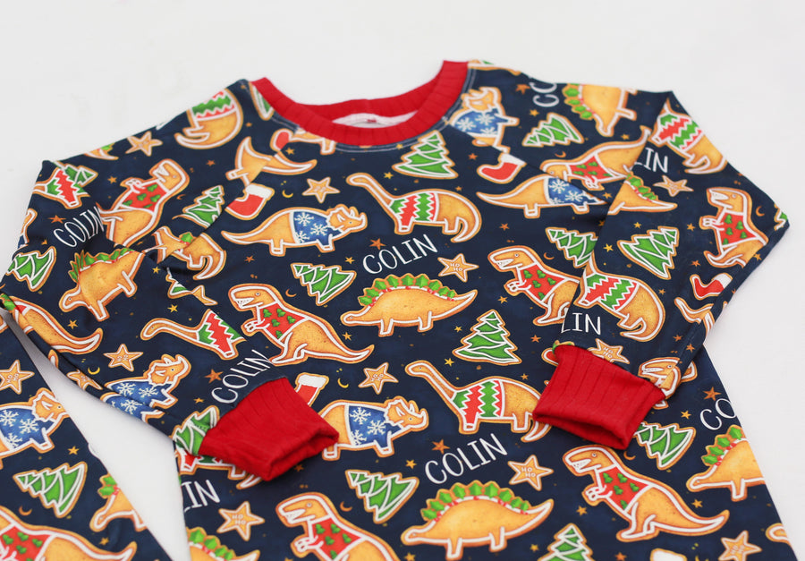 personalized Dino Cookie print Christmas pajamas, navy blue background with dinosaur shaped cookies wearing Christmas sweaters