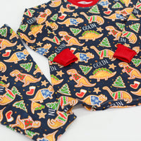 Little boy wearing personalized Dino Cookie print Christmas pajamas, navy blue background with dinosaur shaped cookies wearing Christmas sweaters