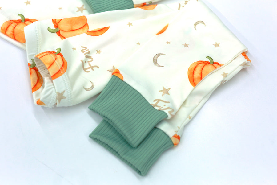 personalized fall pajamas for little boys that have orange cartoon pumpkins and child's name in light brown letters on ivory fabric with green cuffs.