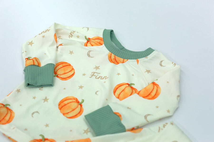 personalized fall pajamas for little boys that have orange cartoon pumpkins and child's name in light brown letters on ivory fabric with green cuffs.