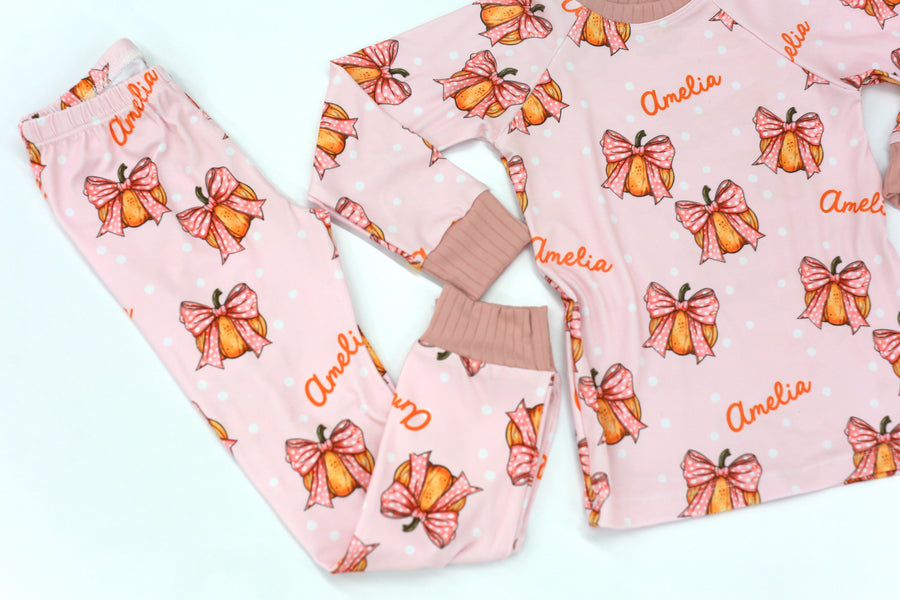 personalized Halloween nightwear for kids, pink pajamas with pumpkins and bows and little girls name, with pink cuffs.