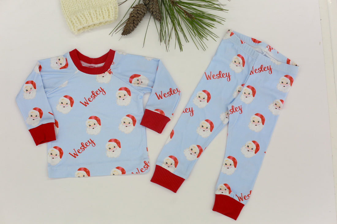 Children's pajama set with Santa Claus pattern on a light blue background, featuring the child's name and red cuffs.