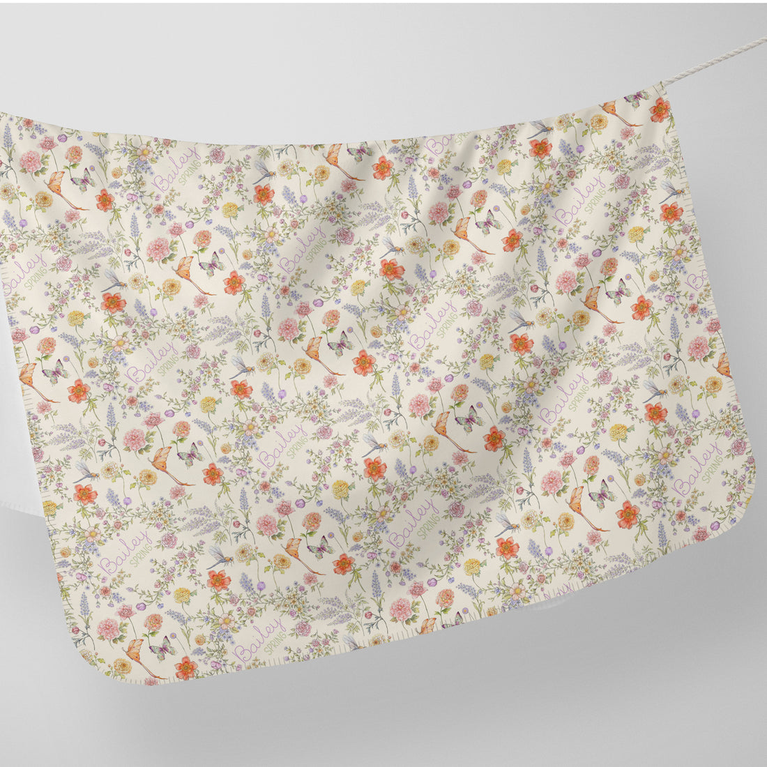 a white fabric with a floral pattern, including various flowers, leaves, and butterflies. The fabric appears to be hanging on a line, creating a visually appealing and decorative piece.