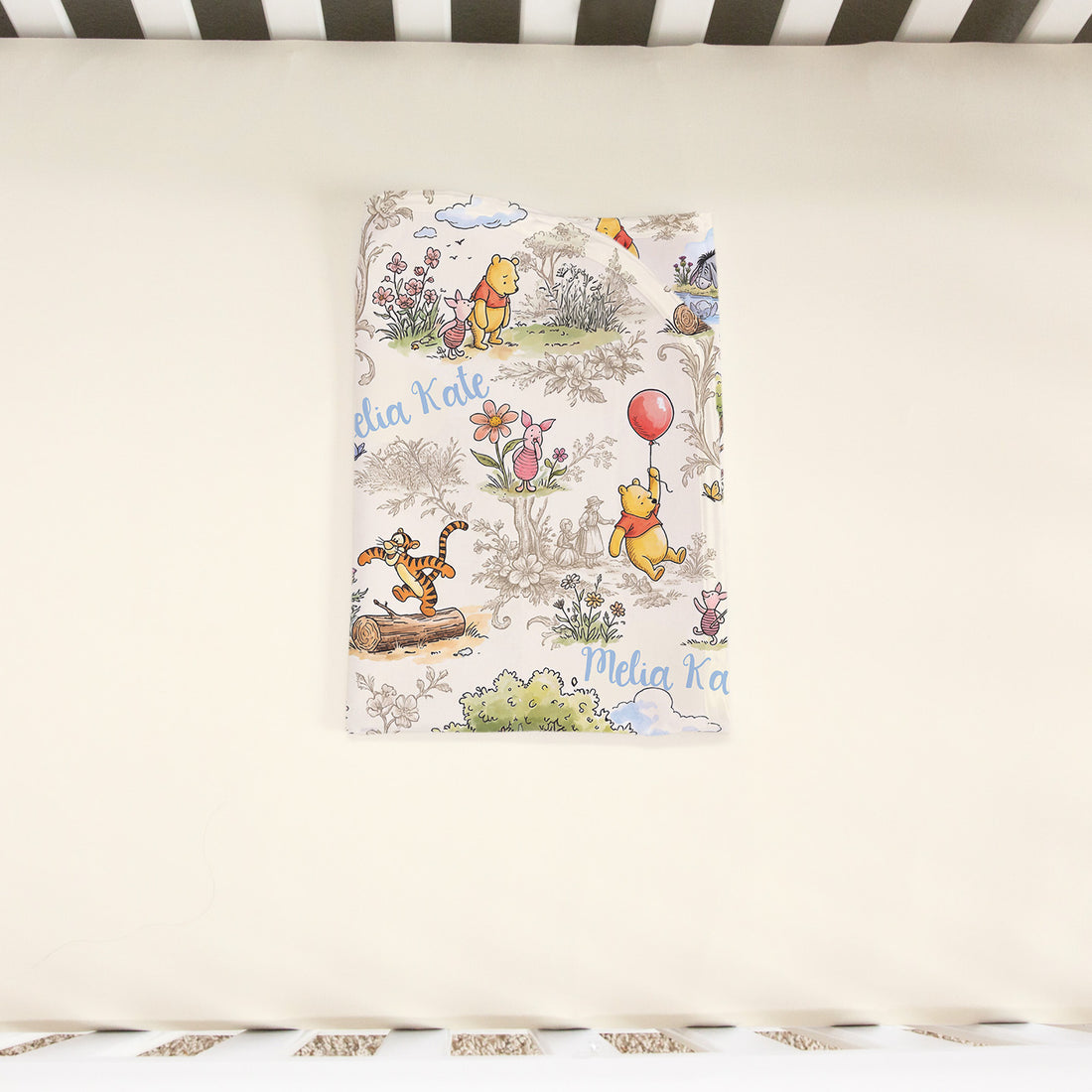 A Winnie the Pooh themed bedding set with illustrations of the characters and the text "Melinda Kate" printed on it.