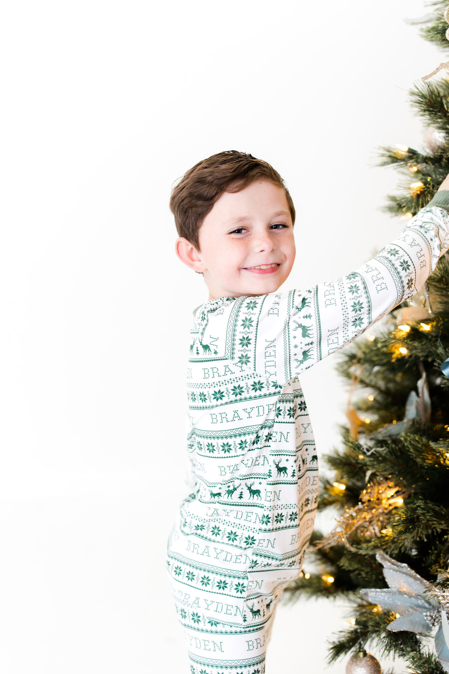 little boy wearing personalized Christmas pajamas in a  green knit stripe print and child's name on a white background and red cuffs.