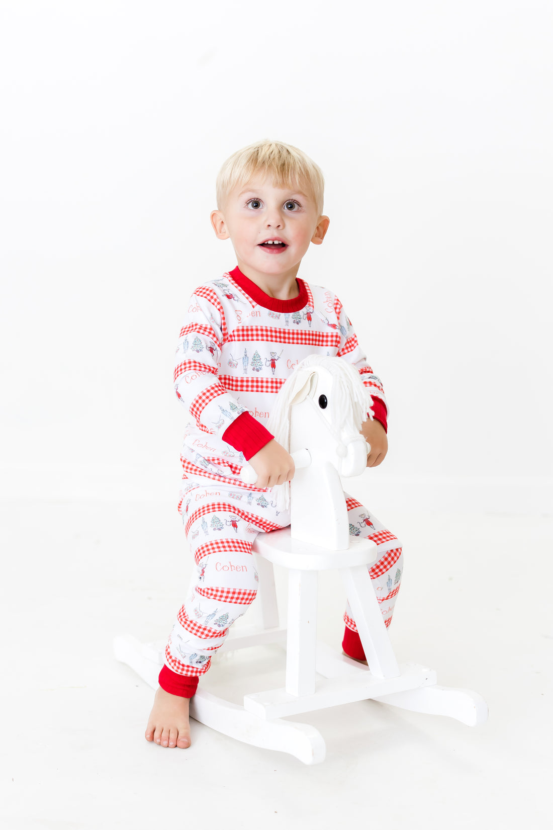 Little boy wearing personalized Modern Nutcracker Ballet for little boys with minimalistic images from the Nutcracker Ballet and his name with red checkered stripe pattern on white background and red cuffs.