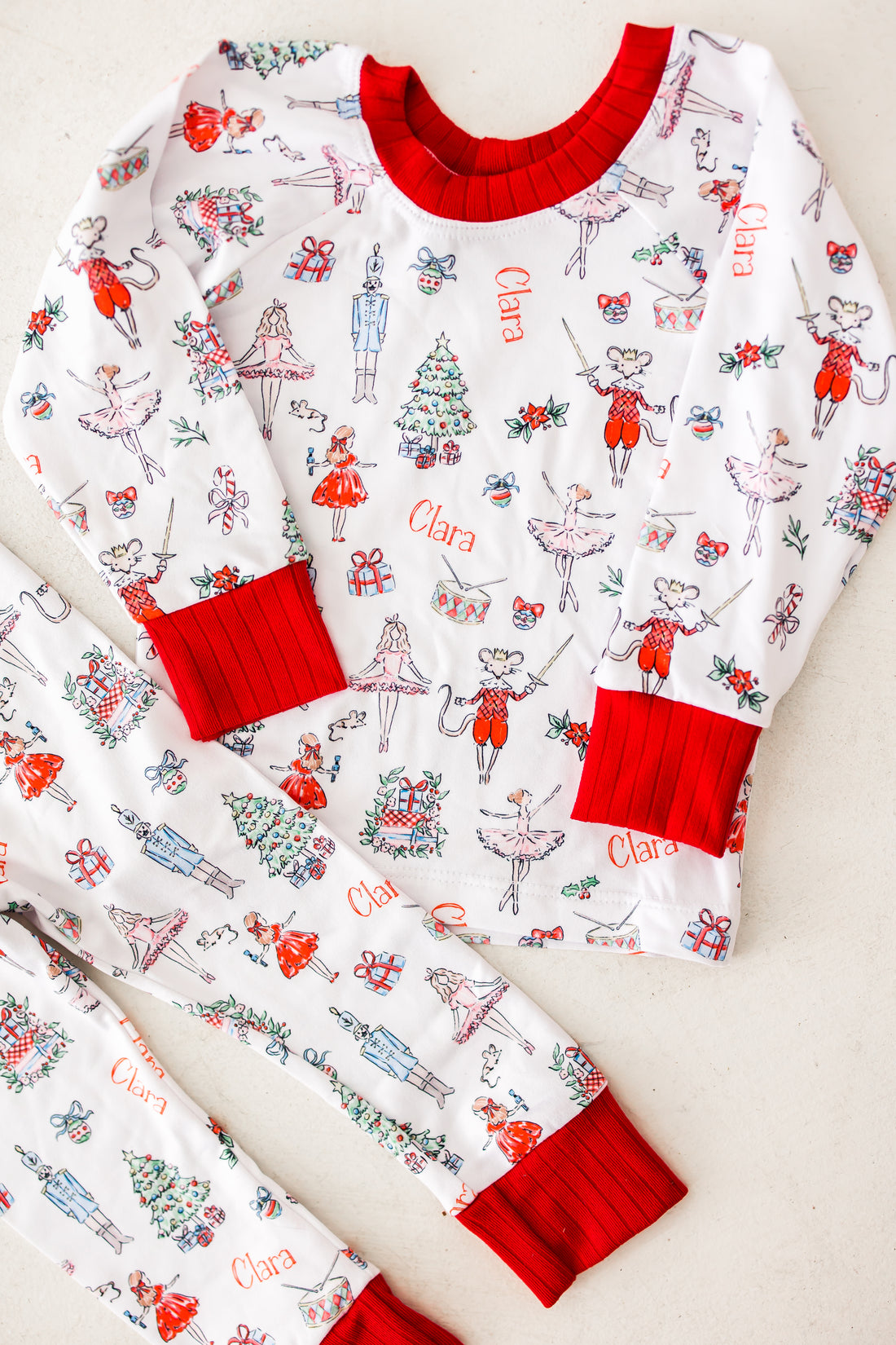 personalized Modern Nutcracker Ballet pajamas, featuring minimalistic images from the iconic nutcracker ballet among child's name on white fabric with red cuffs. 