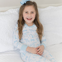 little girl wearing personalized little girl pjs with light blue bows and monogrammed initials on a white background and light blue cuffs. 
