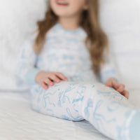 little girl wearing personalized little girl pjs with light blue bows and monogrammed initials on a white background and light blue cuffs. 