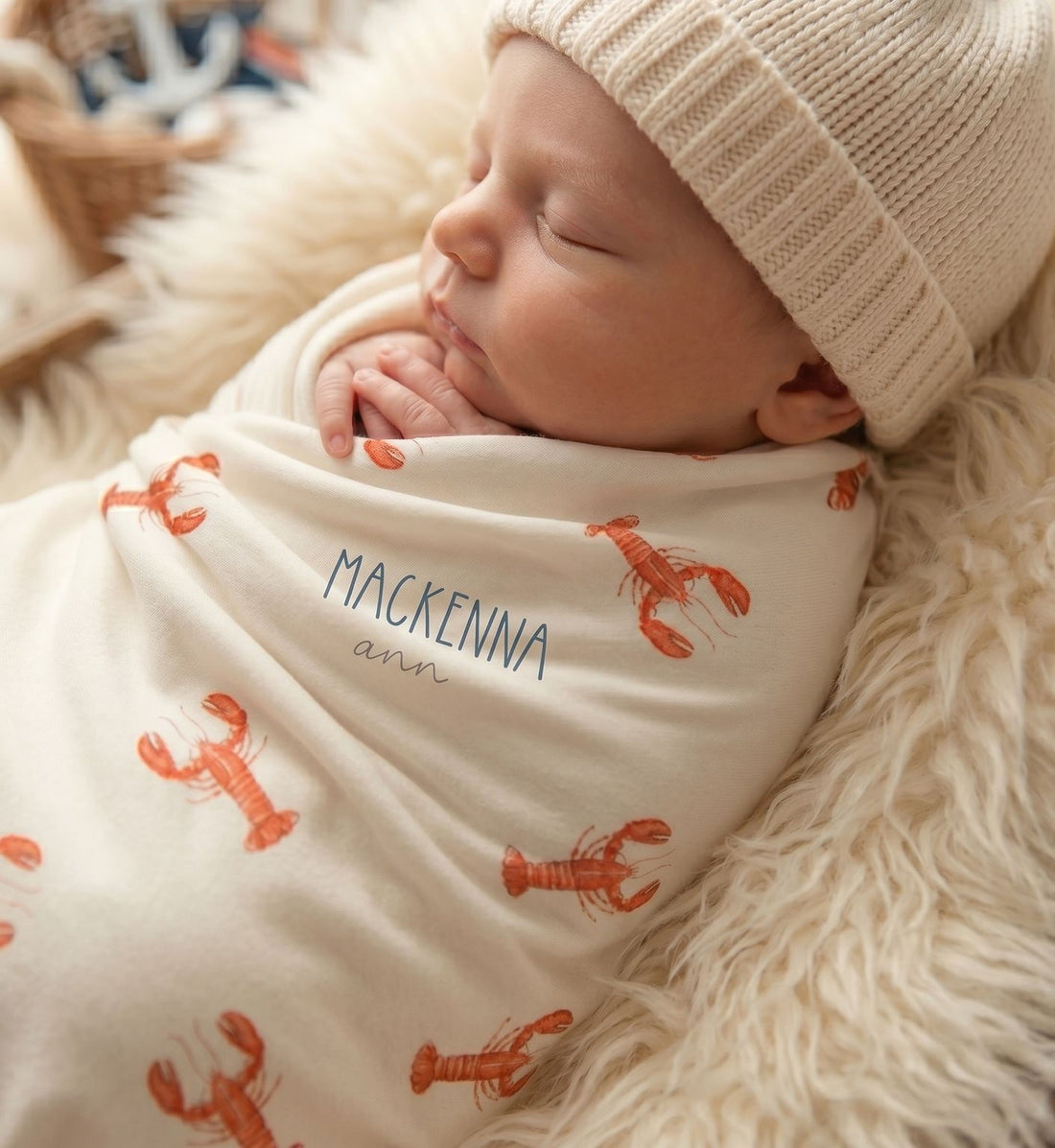 A sleeping newborn baby wrapped in a blanket with a lobster pattern, wearing a white knit cap.
