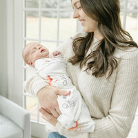 A woman in a white sweater holds a sleeping newborn baby wrapped in a blanket with the name "Caleb" printed on it.
