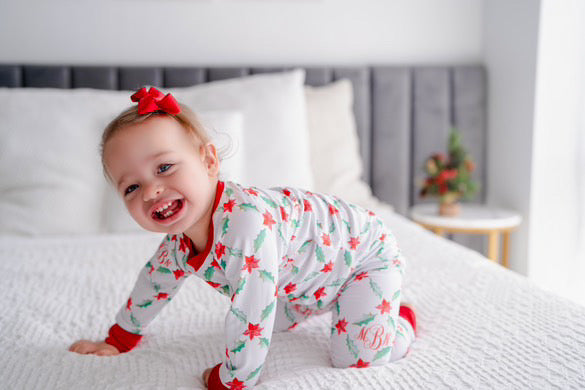 LIttle girl wearing personalized Holiday Pajamas for Girls with coquette style lattice holly leaf print, red ribbins, and initials monogrammed in red, on white jersey knit background and red cuffs.