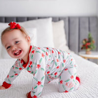 LIttle girl wearing personalized Holiday Pajamas for Girls with coquette style lattice holly leaf print, red ribbins, and initials monogrammed in red, on white jersey knit background and red cuffs.