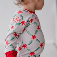 LIttle girl wearing personalized Holiday Pajamas for Girls with coquette style lattice holly leaf print, red ribbins, and initials monogrammed in red, on white jersey knit background and red cuffs.