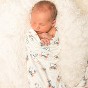 Newborn baby wrapped in a swaddle with crab pattern on a soft white blanket