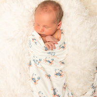 Newborn baby wrapped in a swaddle with crab pattern on a soft white blanket