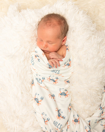 Newborn baby wrapped in a swaddle with crab pattern on a soft white blanket