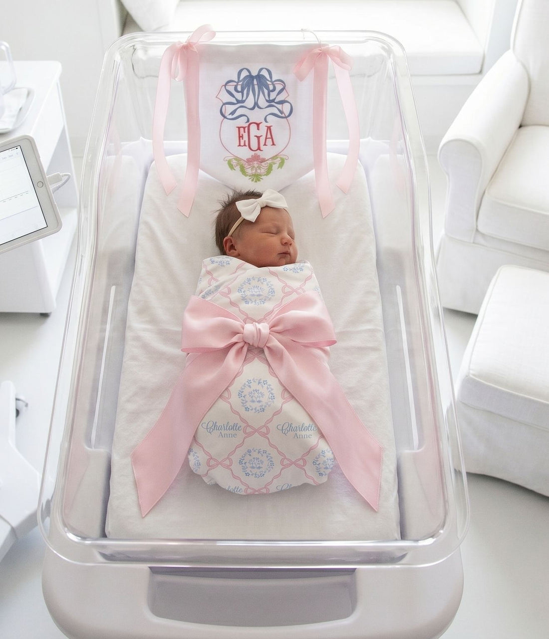 A newborn baby girl is peacefully sleeping in a hospital bed, wrapped in a pink blanket and adorned with a pink ribbon.