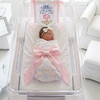 A newborn baby girl is peacefully sleeping in a hospital bed, wrapped in a pink blanket and adorned with a pink ribbon.