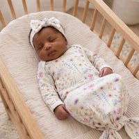 A newborn baby girl is peacefully sleeping in a wooden crib, wearing a white onesie with a floral pattern and a matching headband.