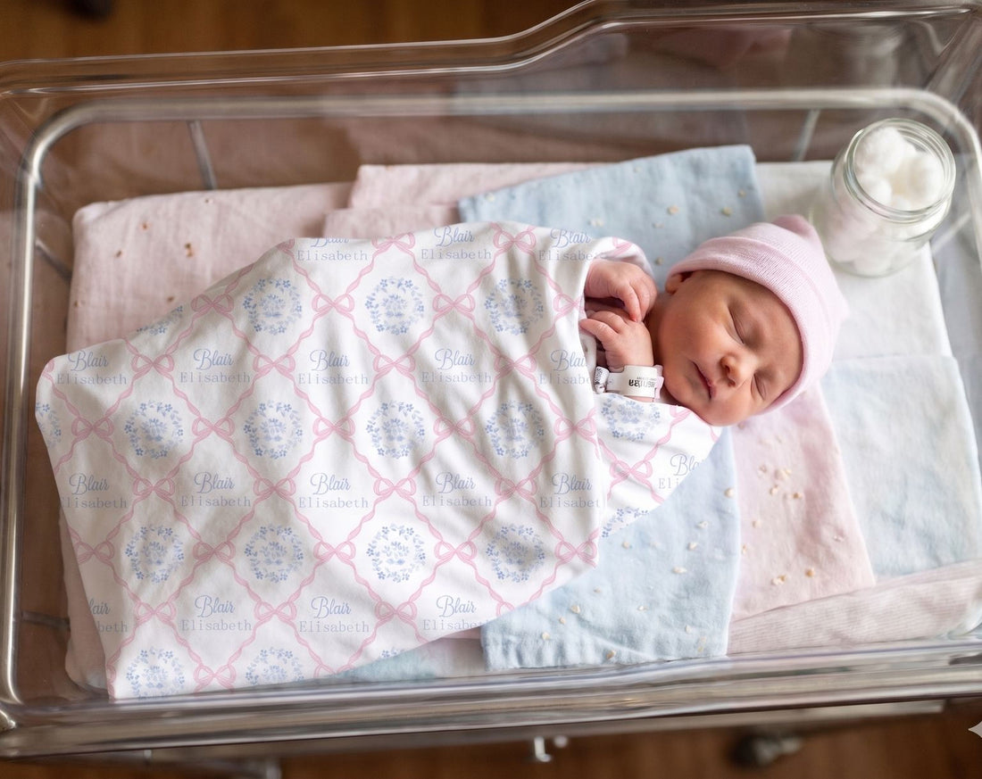 A newborn baby girl is peacefully sleeping in a hospital bed, wrapped in a blanket with the name 'Eliza' printed on it.