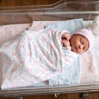 A newborn baby girl is peacefully sleeping in a hospital bed, wrapped in a blanket with the name 'Eliza' printed on it.