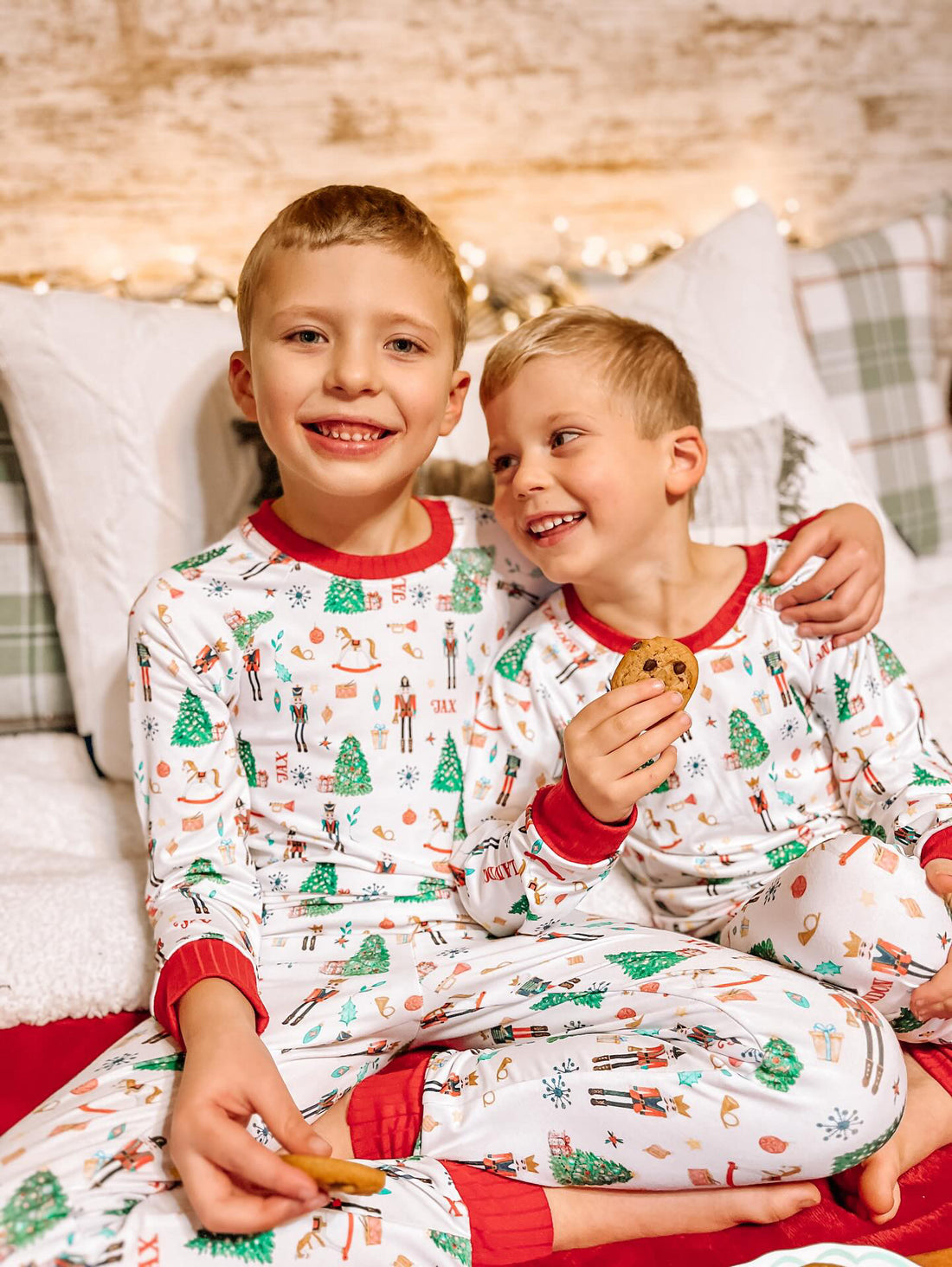 little boys wearing personalized Christmas pajamas featuring classic nutcracker images along with kid's name on white material and red cuffs.