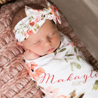 A newborn baby girl is peacefully sleeping in a basket, wearing a white floral headband and a blanket with the name "Makayla" printed on it.