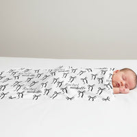 A newborn baby is peacefully sleeping on a bed, wrapped in a blanket with the name "Rachael" and "Michael" printed on it.