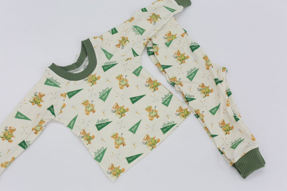 A pair of pajamas with a repeating pattern of green and white teddy bears on a white background.