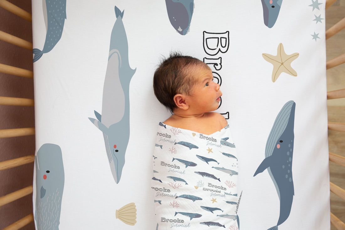 A baby is lying in a crib, wrapped in a blanket with a whale and starfish design.
