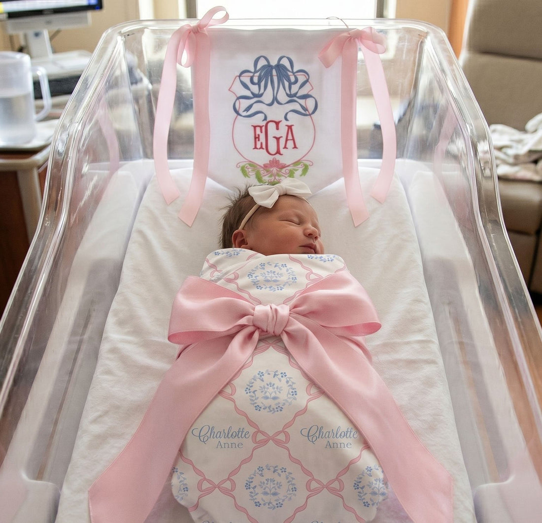 A newborn baby girl is peacefully sleeping in a hospital bed, wrapped in a pink blanket with a large pink ribbon.