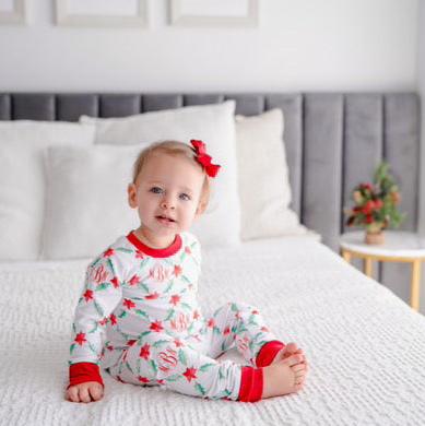 LIttle girl wearing personalized Holiday Pajamas for Girls with coquette style lattice holly leaf print, red ribbins, and initials monogrammed in red, on white jersey knit background and red cuffs.