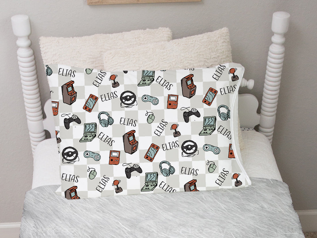 video gamer print personalized pillowcase for kids, light gray checkered background with gaming images such as remotes, consoles, headphones, and tablets in a sketched cartoon style with kid's name.