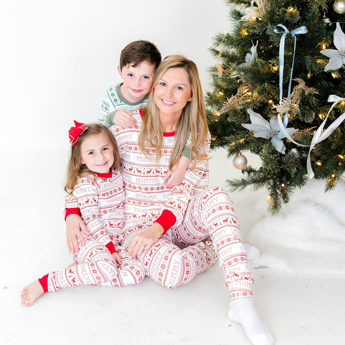 Family wearing matching striped Christmas pajamas sitting in front of the Christmas tree. 