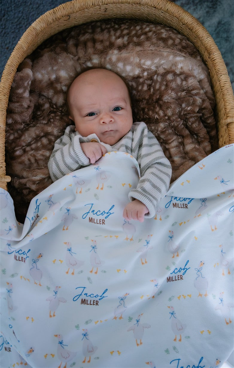 soft white baby blanket with geese and personalized name draped across baby boy in bassinet