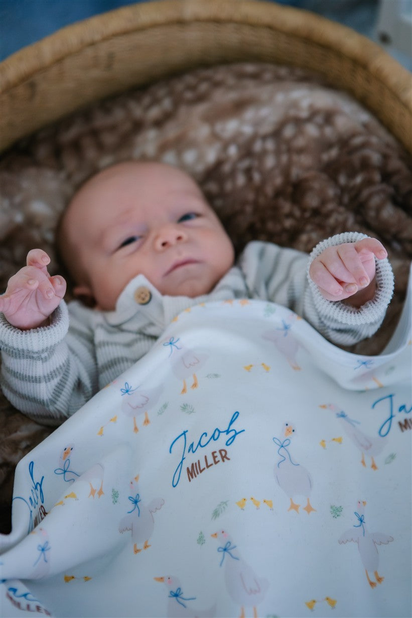 soft white baby blanket with geese and personalized name draped across baby boy in bassinet
