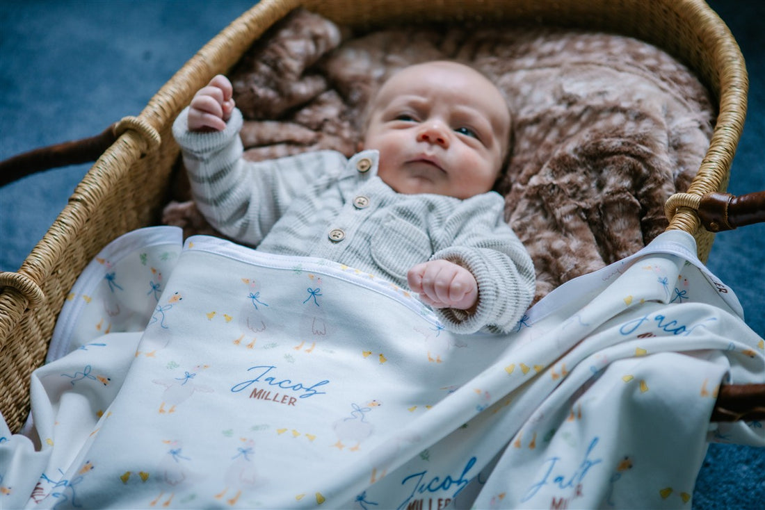 soft white baby blanket with geese and personalized name draped across baby boy in bassinet
