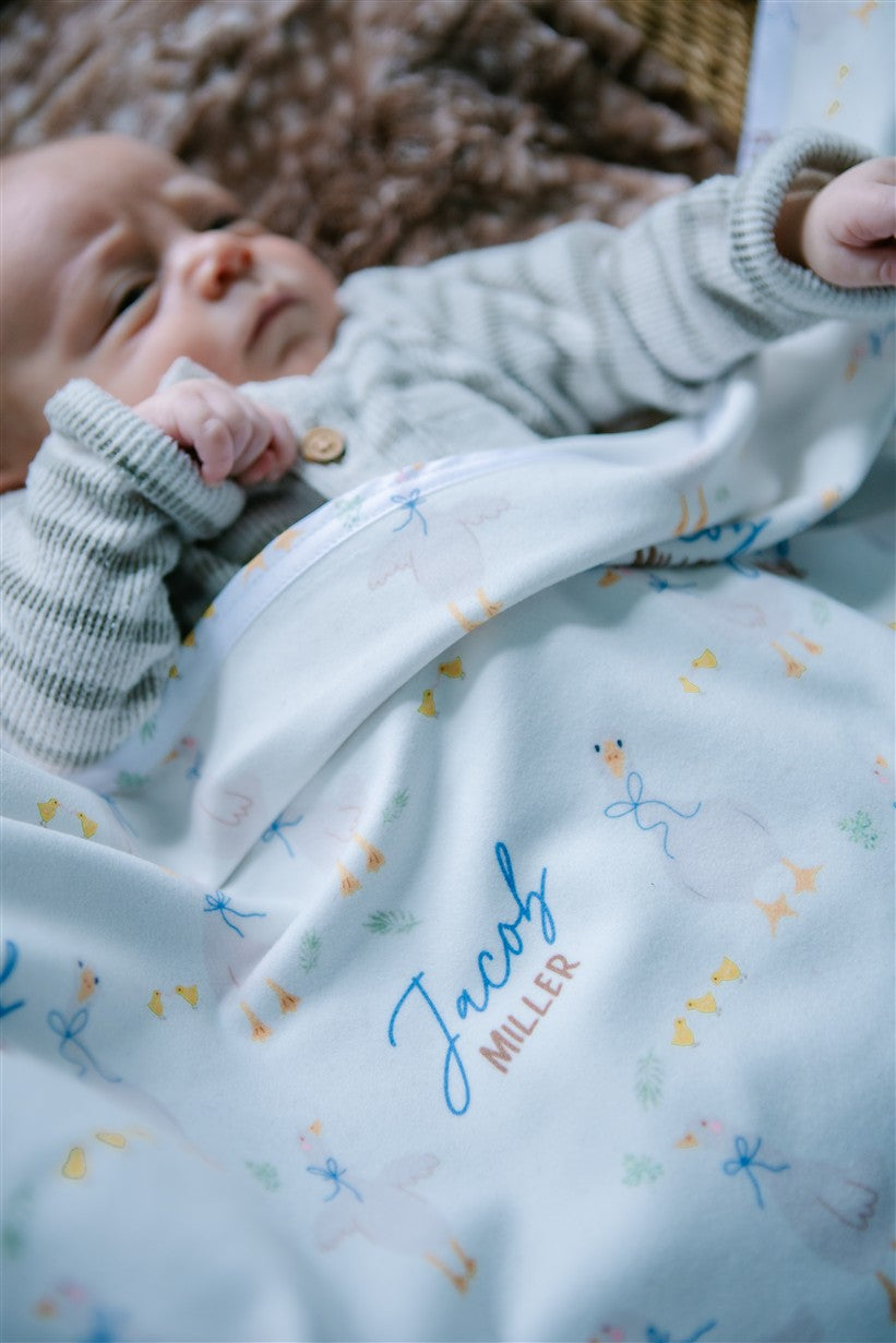 soft white baby blanket with geese and personalized name draped across baby boy in bassinet