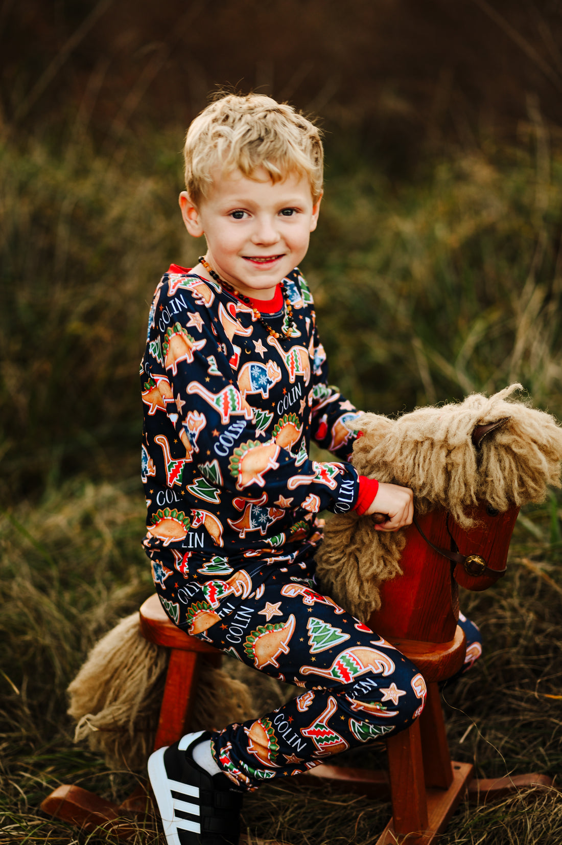 Little boy wearing personalized Dino Cookie print Christmas pajamas, navy blue background with dinosaur shaped cookies wearing Christmas sweaters