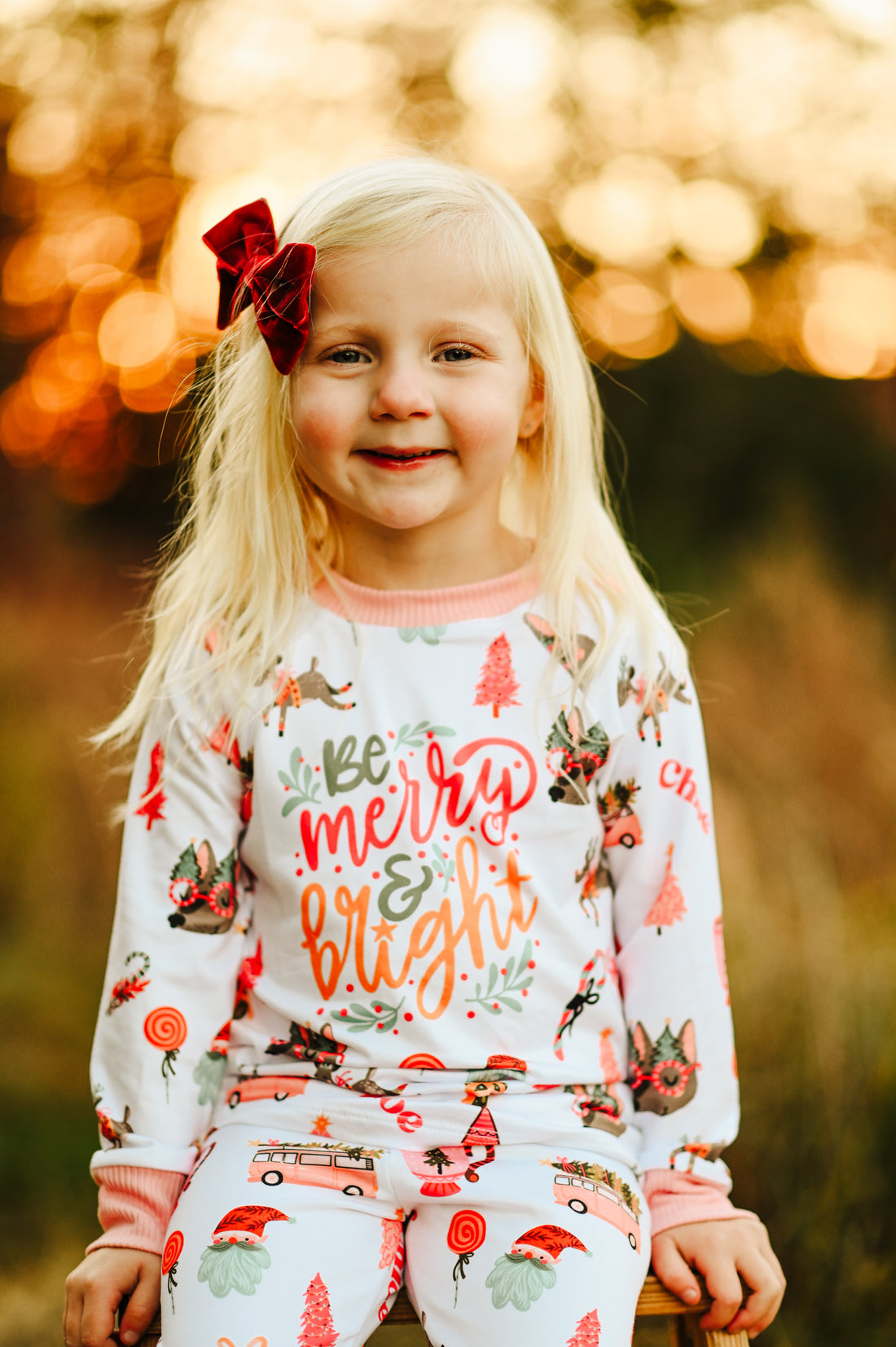 little girl wearing Merry & Bright adorable christmas pajamas, with pink and green cartoon Holiday images such as trees, lollipops, Santa faces, candy canes and reindeer.