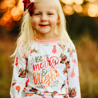 little girl wearing Merry & Bright adorable christmas pajamas, with pink and green cartoon Holiday images such as trees, lollipops, Santa faces, candy canes and reindeer.